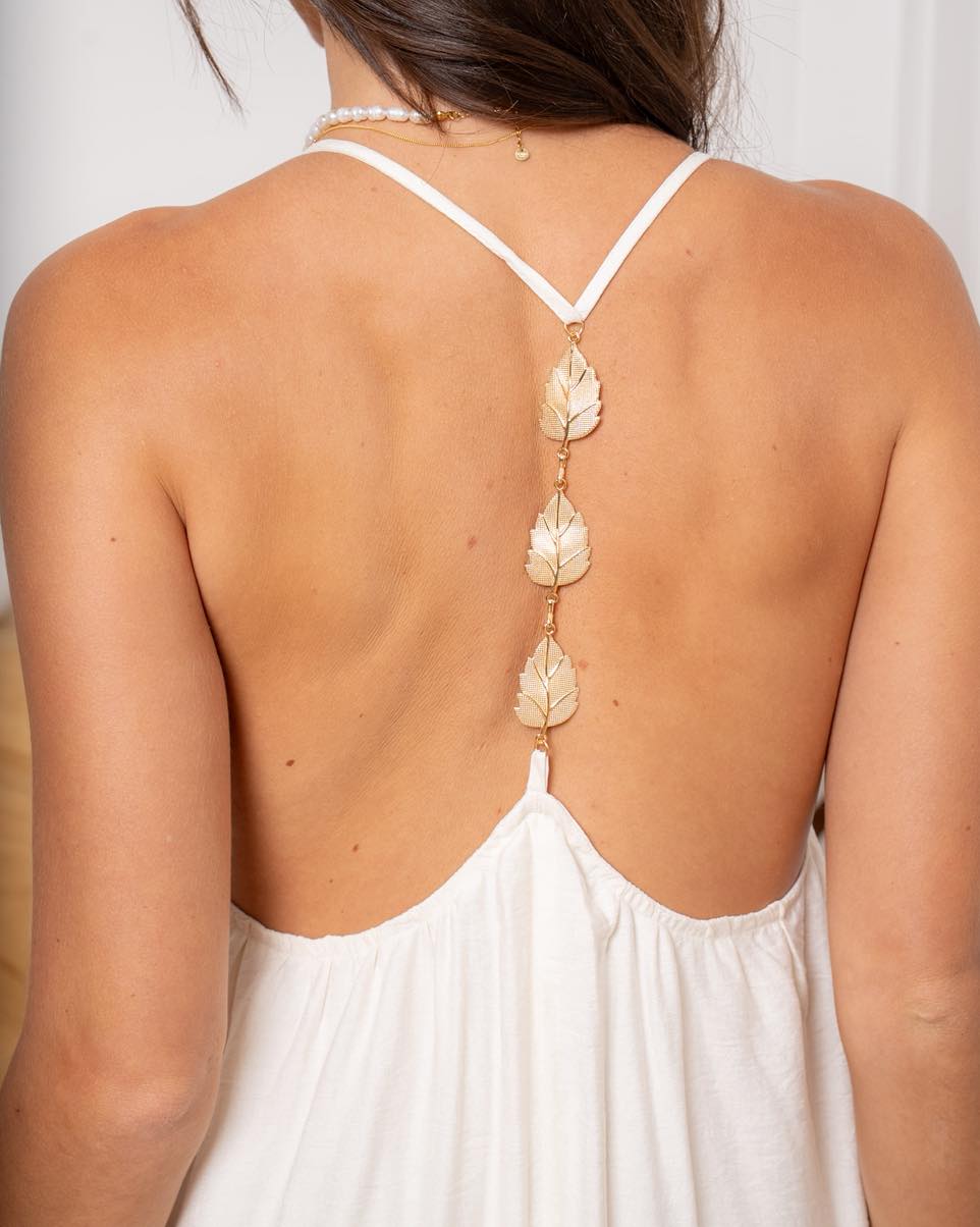 Robe longue fluide blanc écru pour femme avec dos nu orné d’un bijou doré en forme de feuilles, idéale pour une cérémonie ou un mariage.