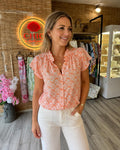 Blouse fluide écrue à imprimé orange corail, col volanté, manches courtes volantées et fermeture boutonnée, portée par un mannequin.